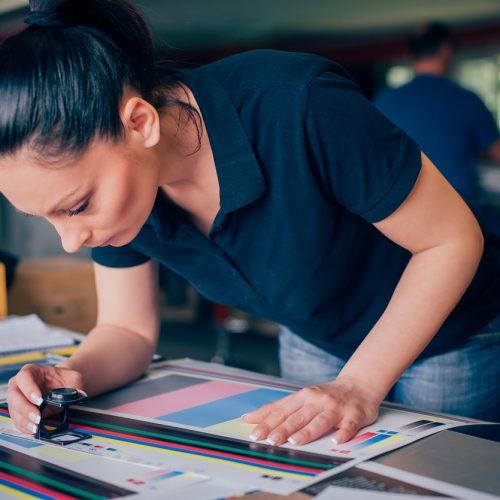 Worker in a printing and press centar uses a magnifying glass and check the print quality